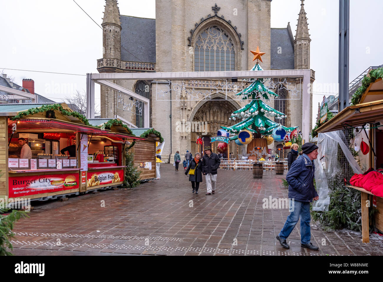 Mercatino di Natale con albero di Natale in piazza prima della Cattedrale di San Bavone entrata. Le persone che frequentano il mercatino di Natale a inizio mattinata nebbiosa Foto Stock