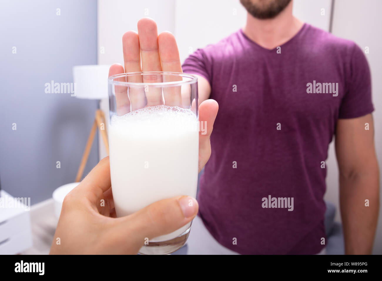 Close-up di un uomo di rigetto di bicchiere di latte offerto da persona a casa Foto Stock