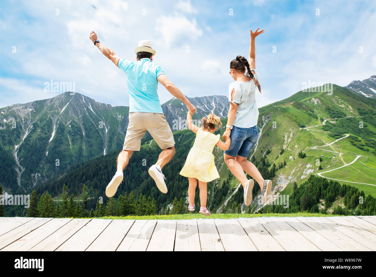 La famiglia felice con la bambina saltando in montagne austriache in estate Foto Stock