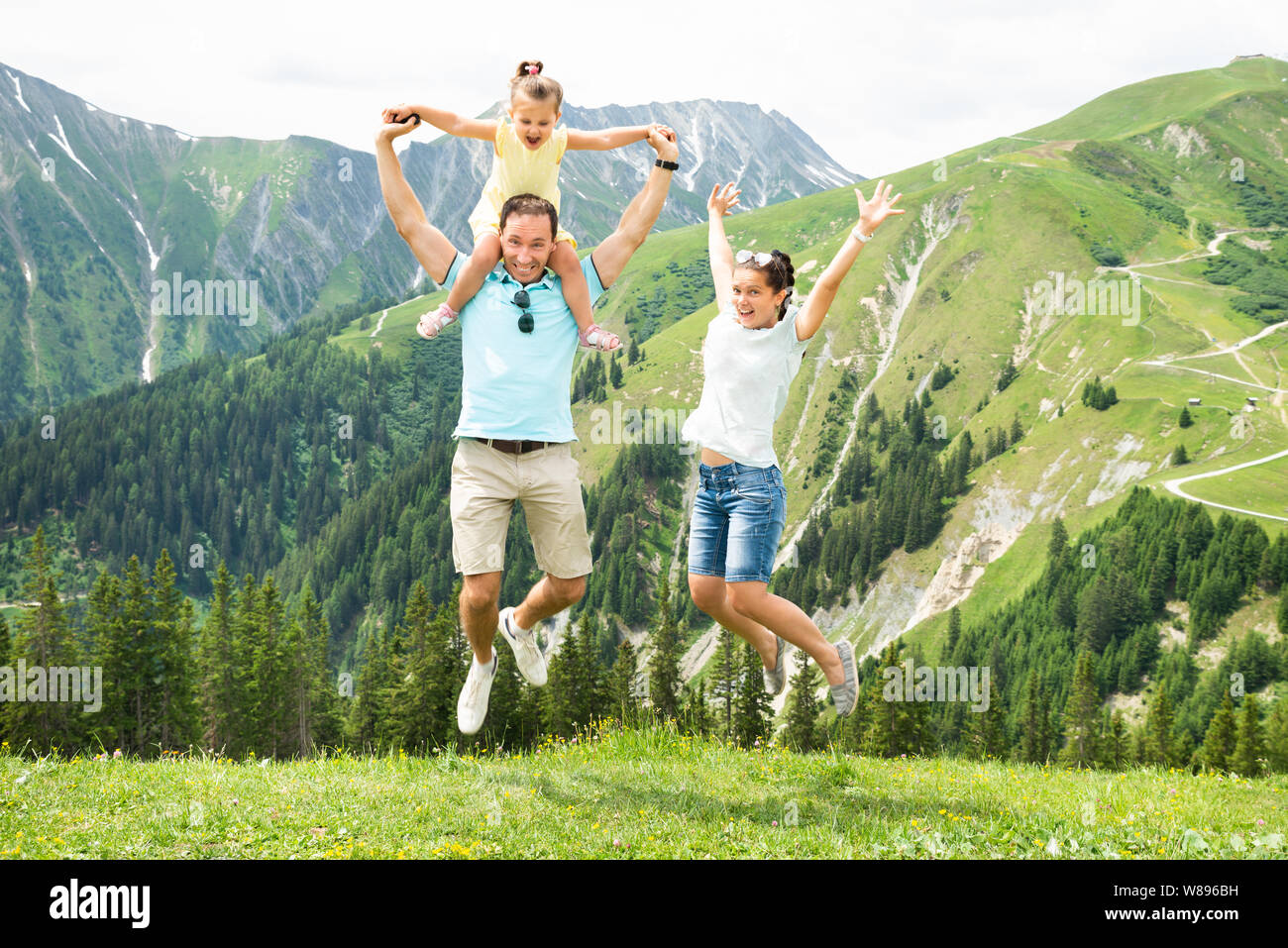 La famiglia felice con la bambina saltando in montagne austriache in estate Foto Stock