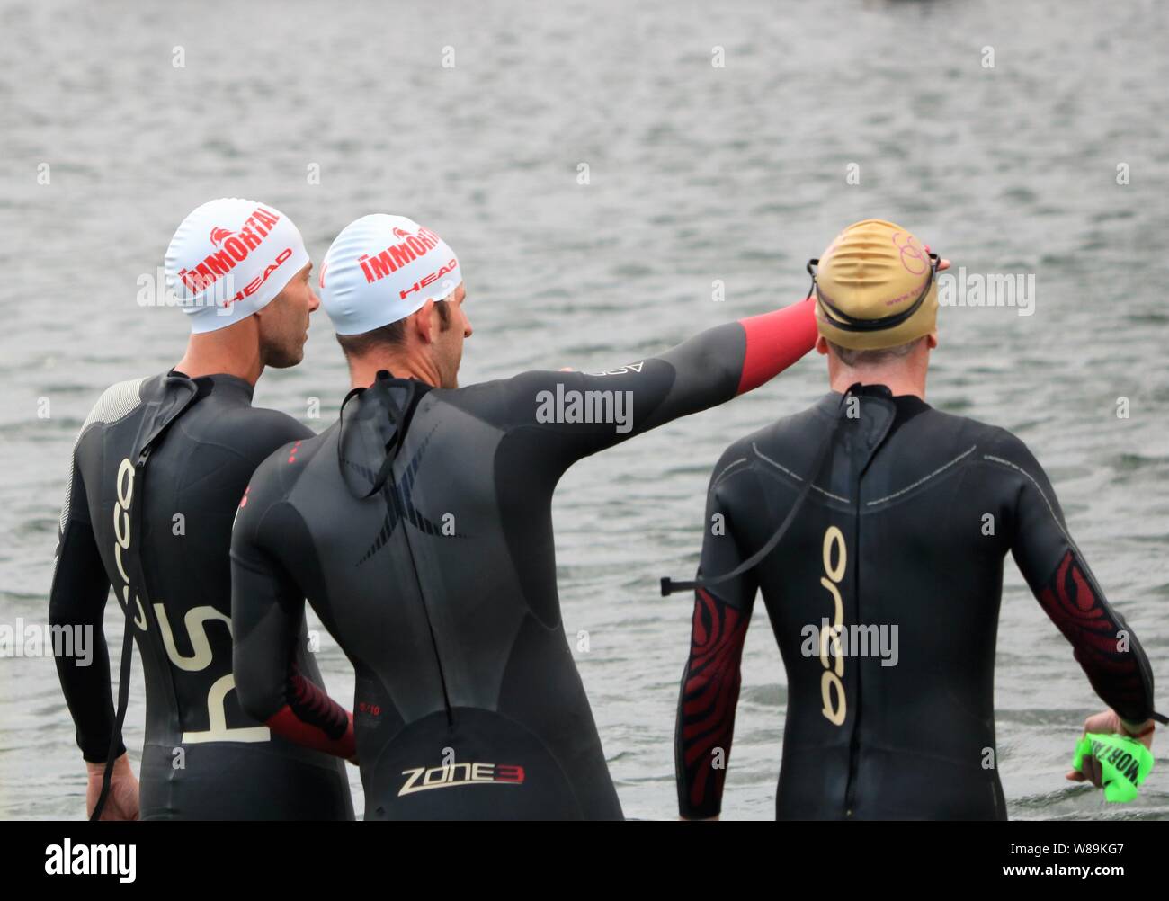 Le persone che hanno preso parte alla volata Farmoor Decathlon, iniziando con l'evento di nuoto, indossando cappelli di nuoto e mute. Foto Stock