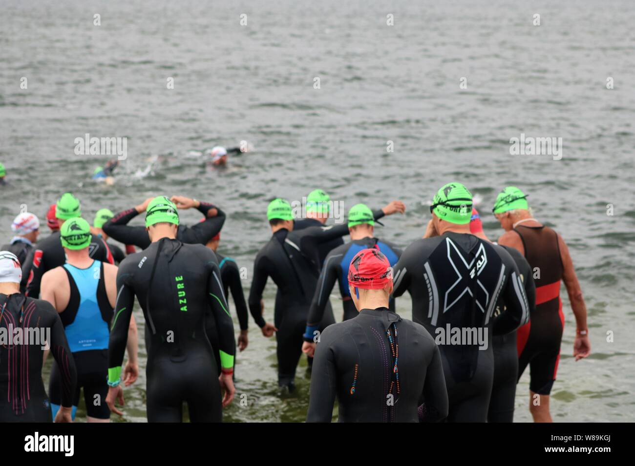 Le persone che hanno preso parte alla volata Farmoor Decathlon, iniziando con l'evento di nuoto, indossando cappelli di nuoto e mute. Foto Stock