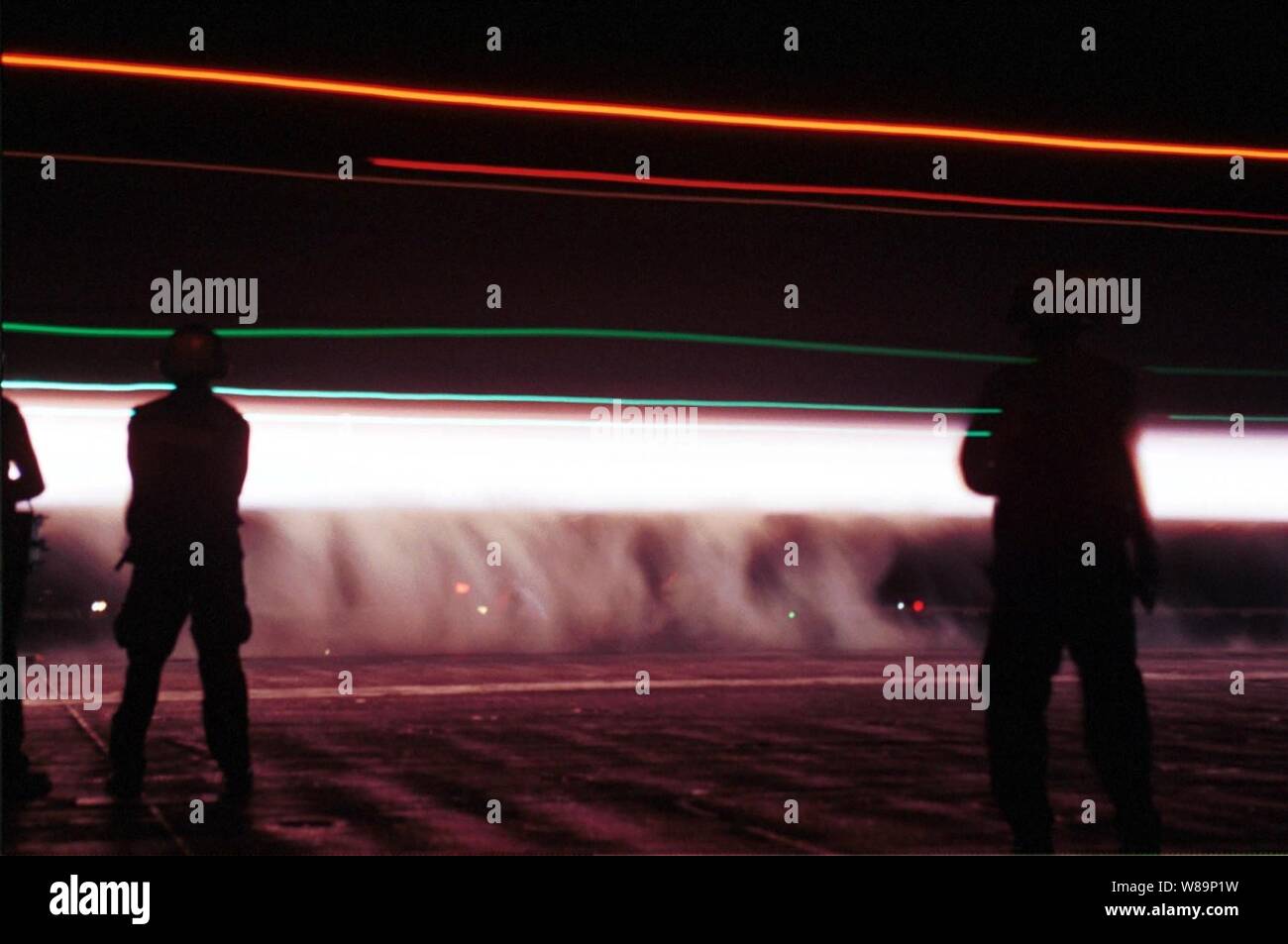 La notte di lancio di un Navy F-14 Tomcat diventa una scia di vapore e luci scontornamento il ponte di volo equipaggio sulla USS Enterprise (CVN 65) il 7 ottobre 2001. L'impresa è il lancio di aerei per colpire le missioni contro al Qaeda terroristici dei campi di addestramento e installazioni militari del regime dei talebani in Afghanistan come parte dell'Operazione Enduring Freedom. La attentamente le azioni mirate sono state progettate per interrompere l'uso dell'Afghanistan come una base per azioni terroristiche e di attaccare le capacità militari del regime dei talebani. Foto Stock