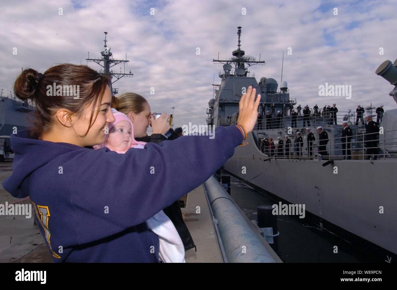 Veronica Rand (sinistra), Teresa Trowbridge (a destra), e figlioccia Kyrsten Trowbridge Wave addio dal molo della stazione navale di San Diego, California, come guardare loro amato Petty Officer di terza classe Tom Rand a bordo della USS Bunker Hill (CG 52) messo in mare su 6 Dicembre 2004. Rand è una marina fire controlman. Foto Stock
