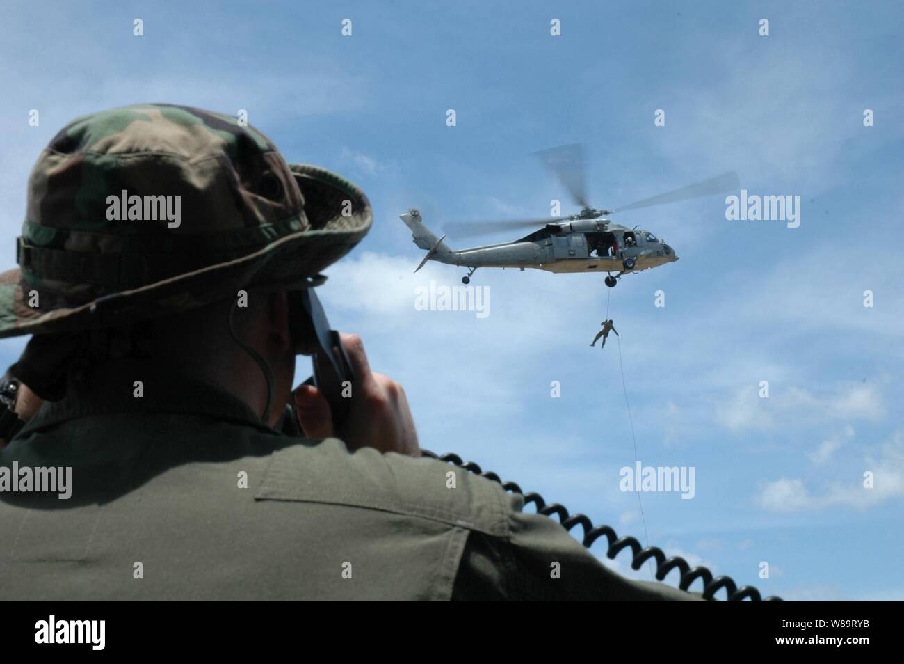 Stati Uniti Navy Petty Officer di 2a classe di Justin Birch utilizza una radio portatile per parlare con i piloti di un MH-60S Seahawk elicottero come l'eliminazione degli ordigni esplosivi tecnico dal Royal Australian Navy respinge dall'elicottero a Santa Rita, Guam, il 19 aprile 2006. I marinai da entrambe le marine sono la formazione in elicottero corda tecniche di sospensione a Santa Rita. Foto Stock