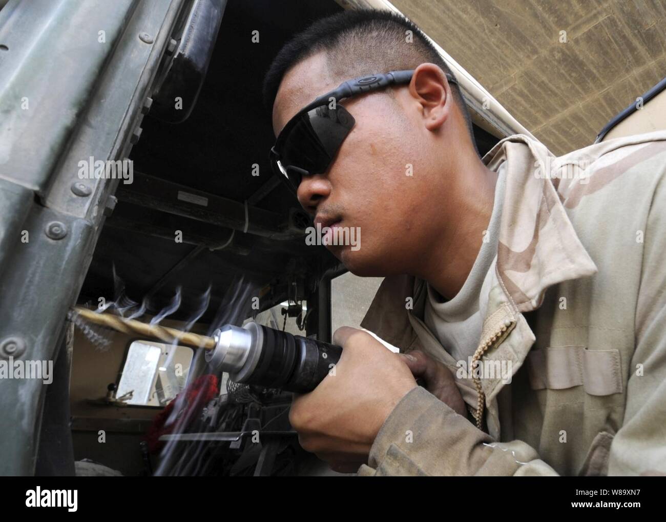 Stati Uniti Army Spc. Richard Cavasug, assegnati al 3° Brigata, 215th brigata battaglione di supporto, 1° Divisione di cavalleria, punte per trapano un foro per sostituire una cerniera su un Humvee porta a una base officina in avanti una base operativa Marez a Mosul, Iraq, il 7 luglio 2009. Foto Stock