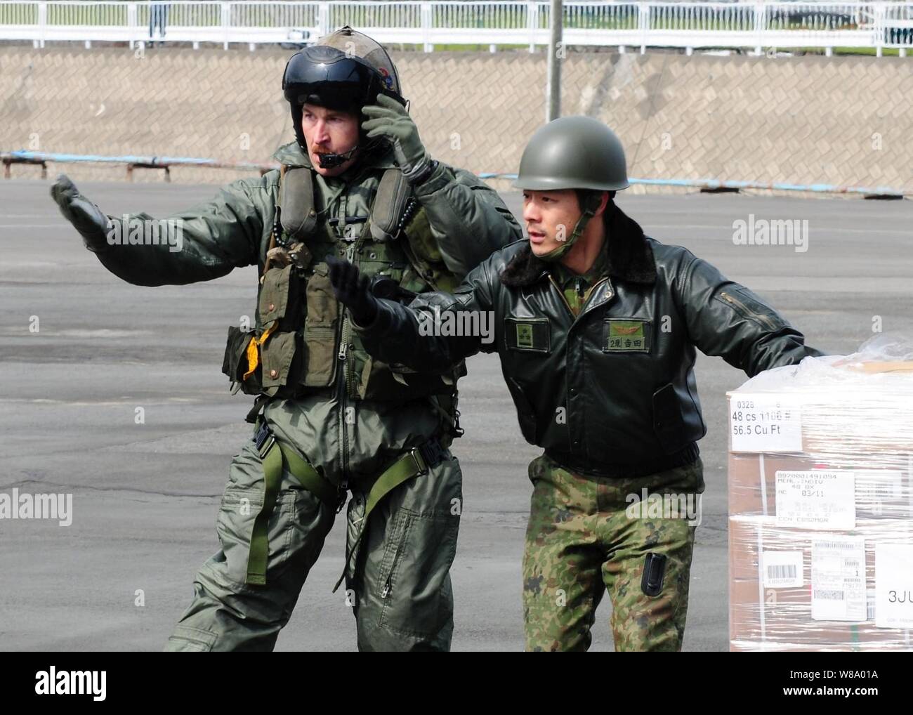 Gunnery Sgt. Sam Carnes (sinistra) e un membro del Giappone di autodifesa marittima diretta della forza del movimento di assistenza umanitaria e di soccorso in caso di catastrofe alimenta scaricata da un CH-46E Sea Knight elicottero assegnato a mezzo marino elicottero Squadron 262, imbarcato a bordo dell'assalto anfibio nave USS Essex (LHD 2) il 22 marzo 2011. L'Essex è operativo al largo della costa di Hachinohe nel nordest del Giappone a sostegno dell'operazione Tomodachi. Foto Stock