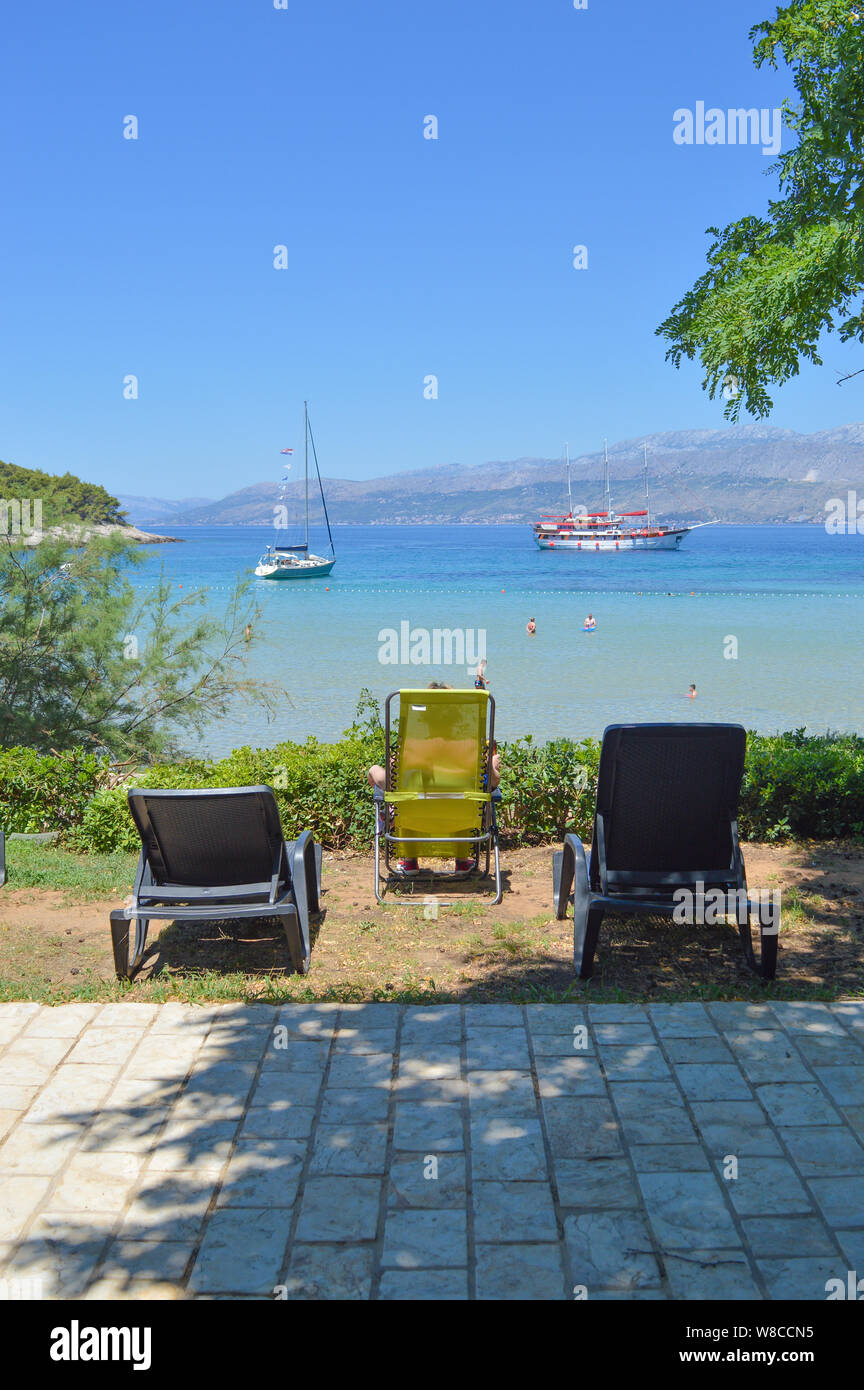 Scena di spiaggia con sedie a sdraio, acqua cristallina e le barche a vela, Lovrečina beach, isola di Brac, Croazia Foto Stock