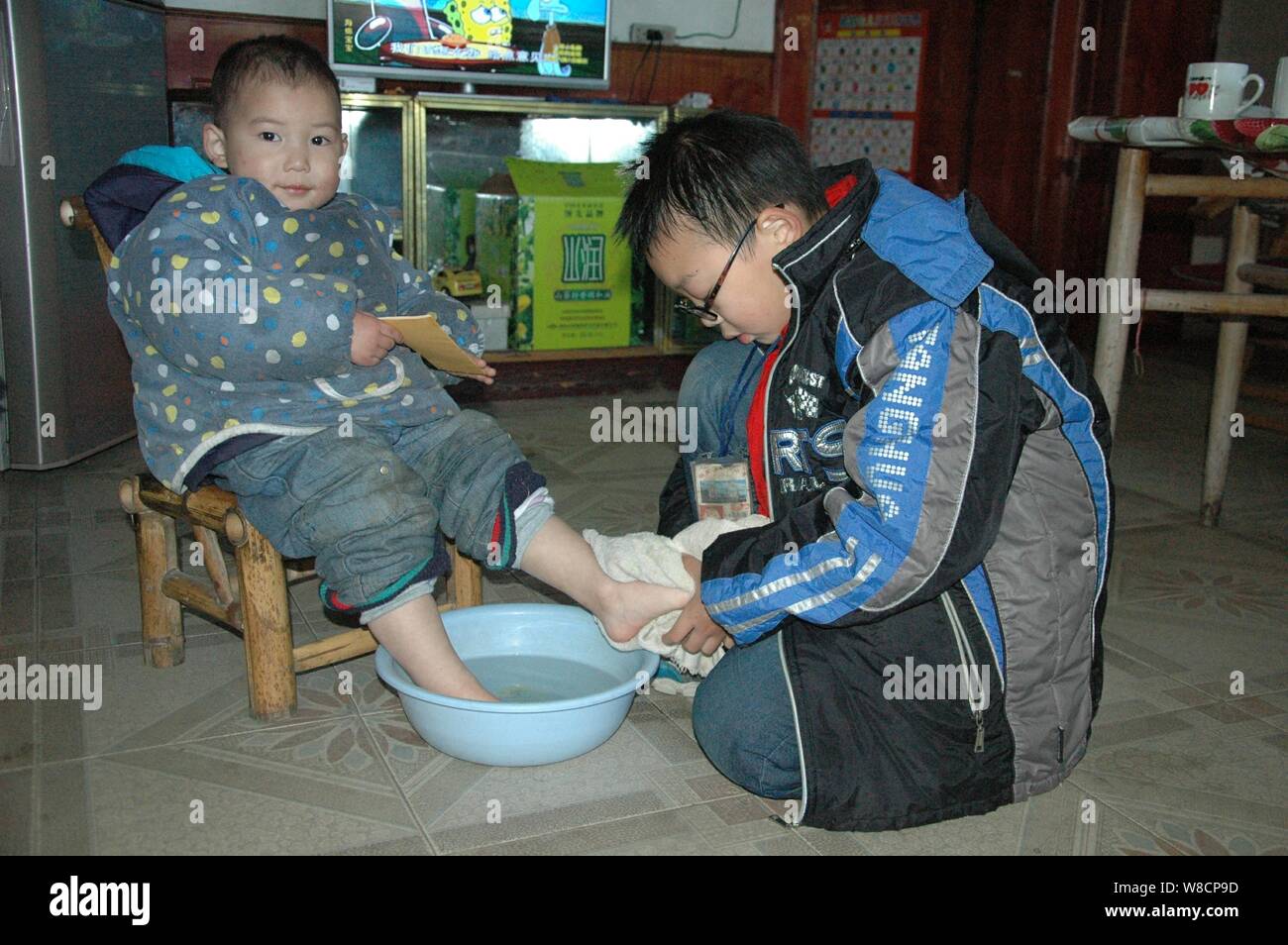 Il 10-anno-vecchio ragazzo Mo Shuangyi, destra lava il suo fratello più giovane i piedi a casa nella contea di Tonggu, Yichun city, Cina orientale della provincia di Jiangxi, 30 Dicembre Foto Stock