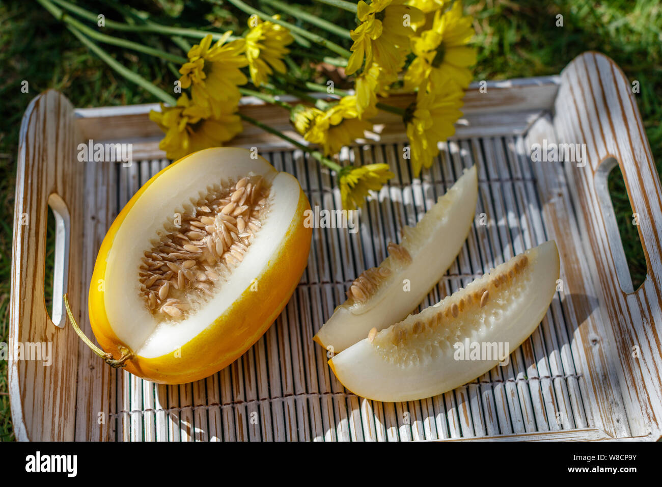 Tagliare giallo melone orientali (Coreano melone) su un bianco vassoio in legno Crisantemo giallo sullo sfondo. Foto Stock