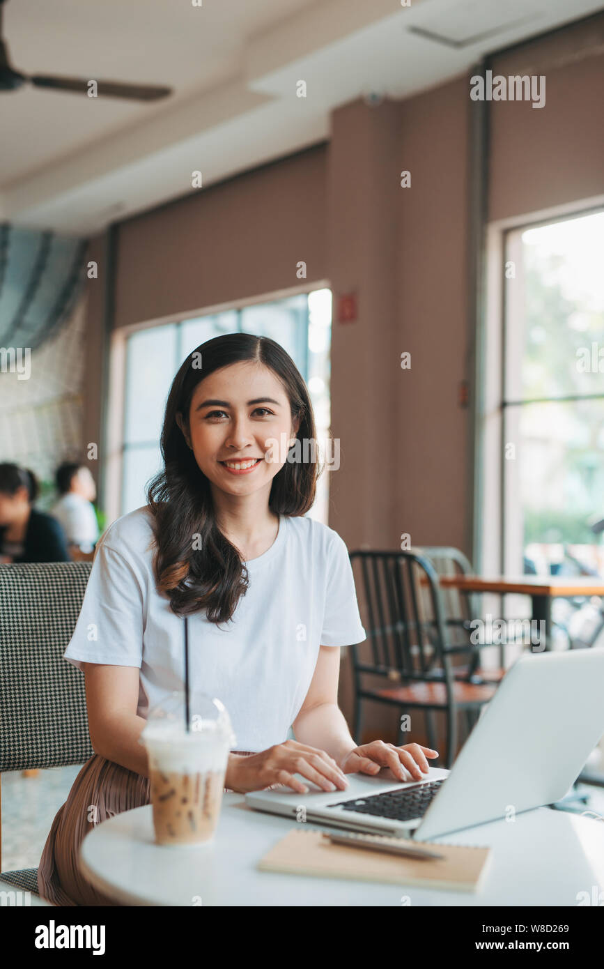 Lifestyle Moda Ritratto di ragazza giovane e carina a lavorare al computer portatile in uno spazio aperto. Bere il caffè. Business donna. Freelance. Foto Stock