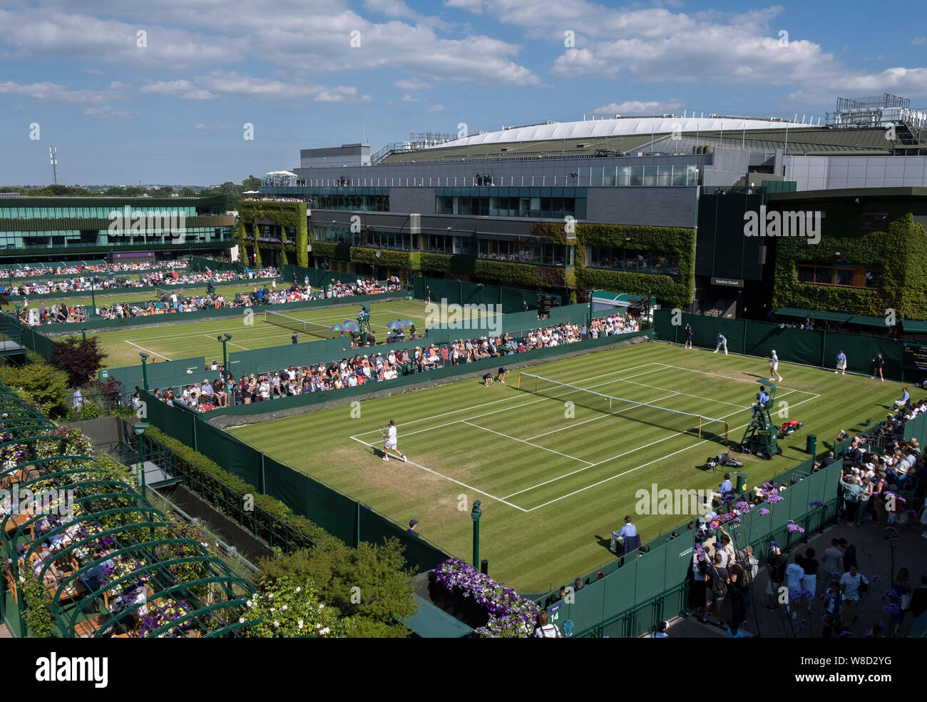 Vista in elevazione di spettatori la visione di gioco al di fuori su corti con corte centrale in background durante il 2019 campionati di Wimbledon, Londra, Inghilterra Foto Stock