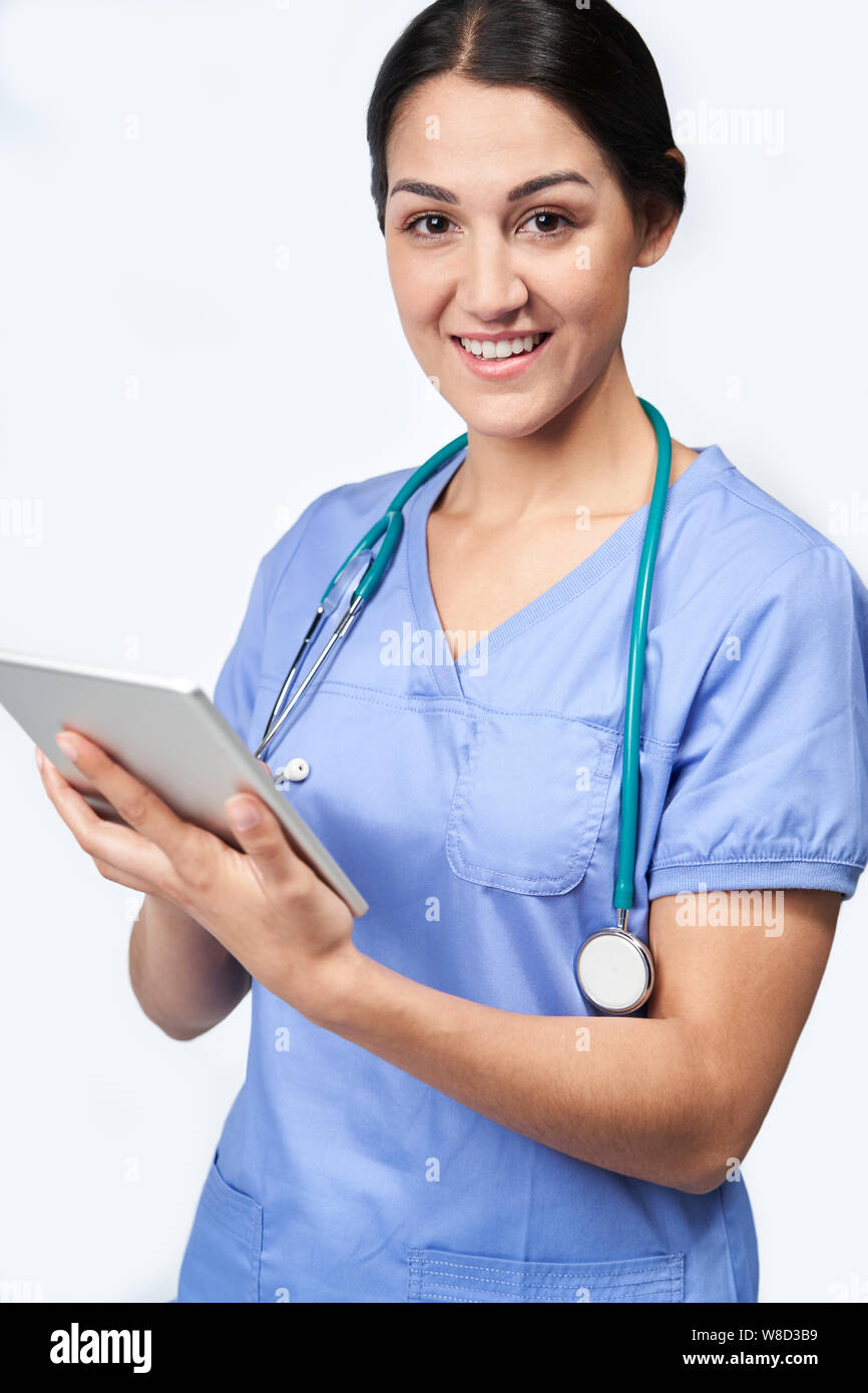 Studio ritratto femminile di infermiere indossando Scrubs utilizzando tavoletta digitale Foto Stock