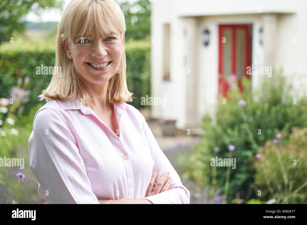 Ritratto di donna matura in piedi nel giardino davanti a casa da sogno in campagna Foto Stock