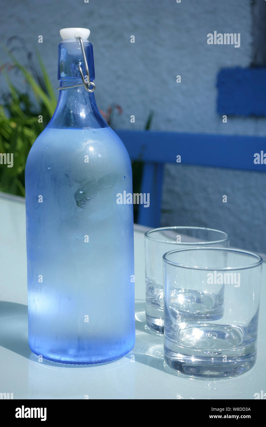 Bottiglia di acqua di rubinetto fredda e due bicchieri su un tavolo da giardino in estate Foto Stock