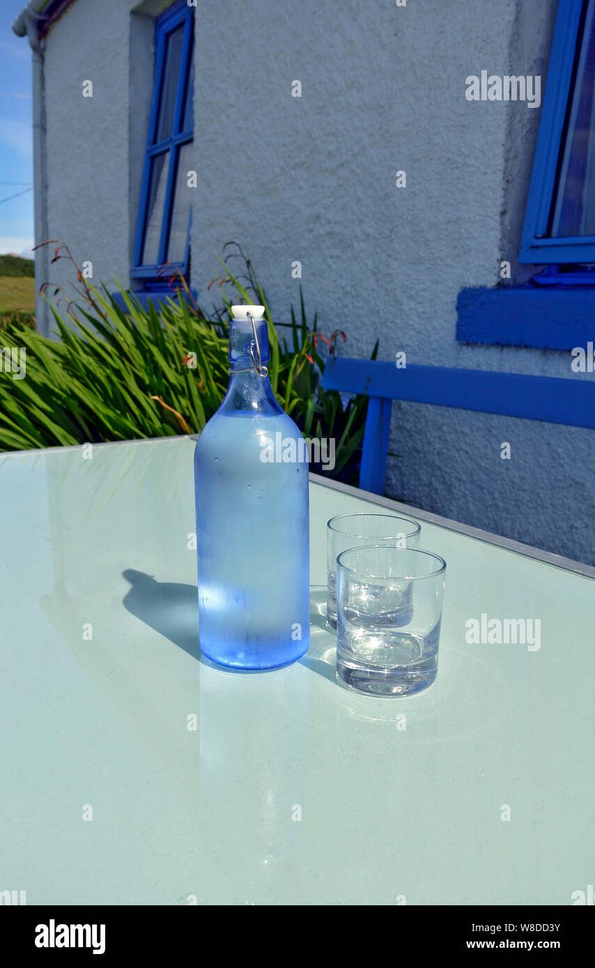 Bottiglia di acqua di rubinetto fredda e due bicchieri su un tavolo da giardino in estate Foto Stock