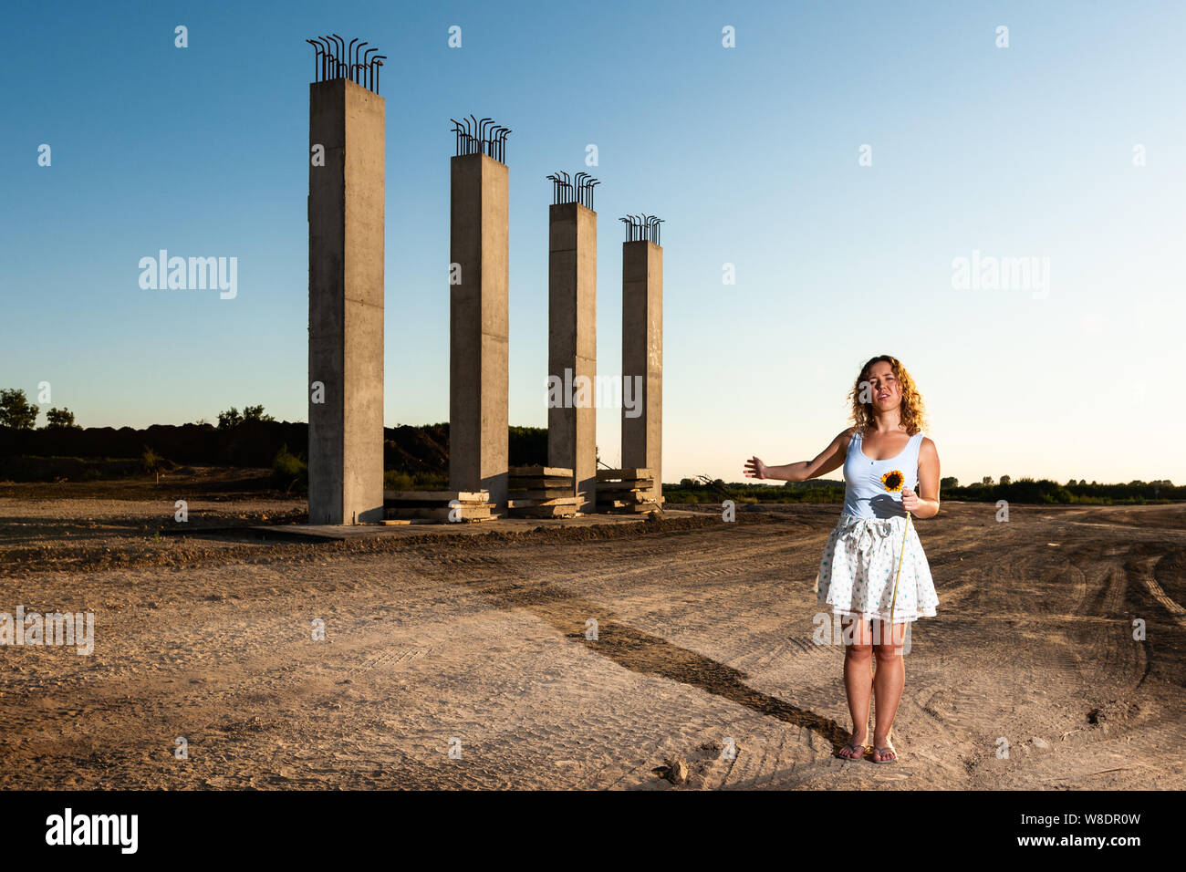 Arrabbiato attivista donna in piedi con girasole morente di fronte a una costruzione di strade. La tutela ambientale concetto. Foto Stock