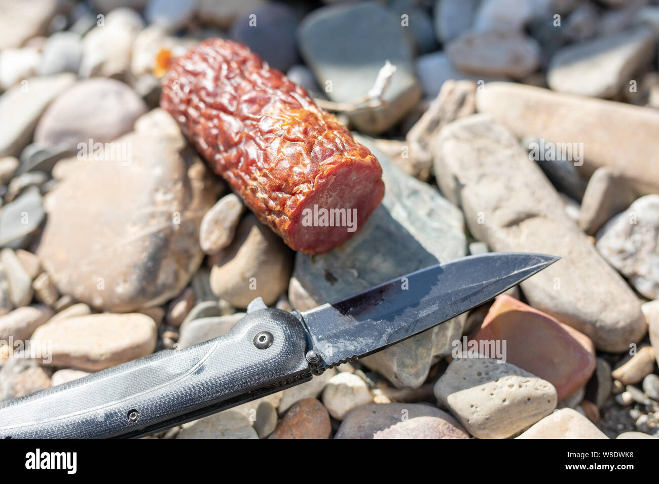Dry-cured salsiccia e un coltello da caccia che giace sulle pietre Snack, cibo camping Foto Stock