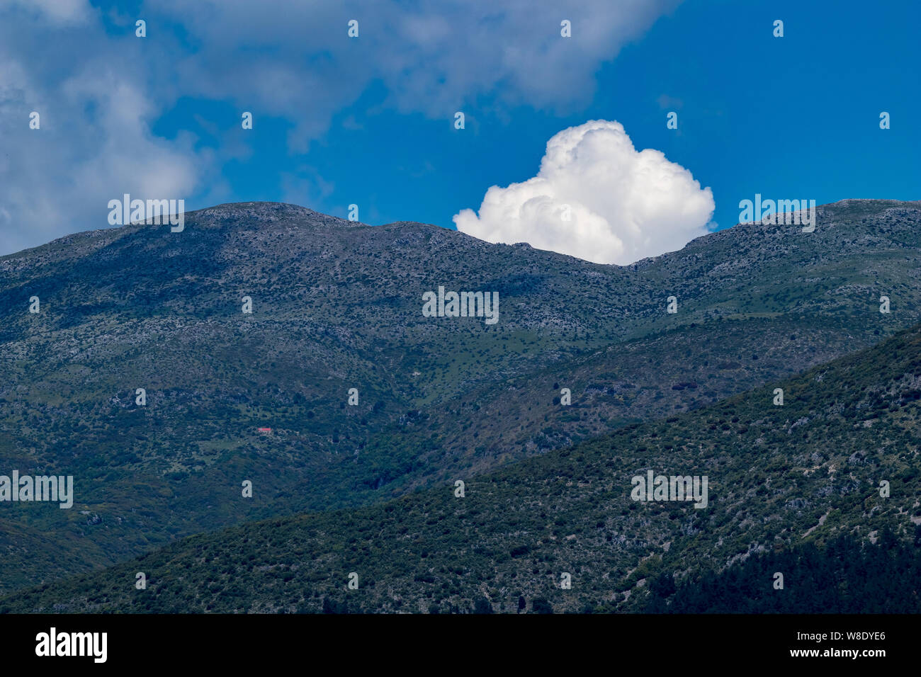 White puffy cloud salta fuori da dietro le cime della montagna vicino alla città di Ioannina, Grecia Foto Stock