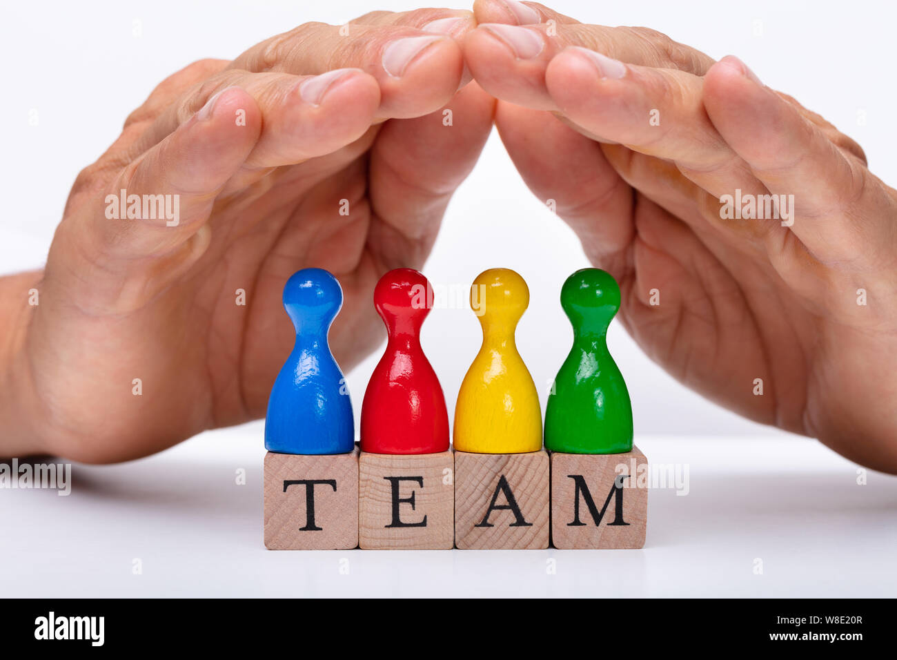 Close-up di un imprenditore la mano della pedina di protezione figure su team di blocchi di legno Foto Stock
