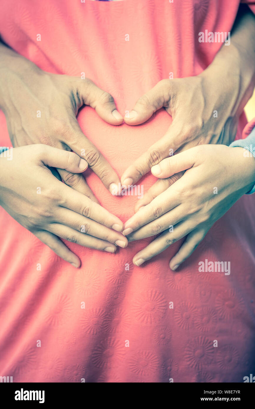 La donna incinta e il marito tenendo le sue mani a forma di cuore sul suo bambino bump. Foto Stock