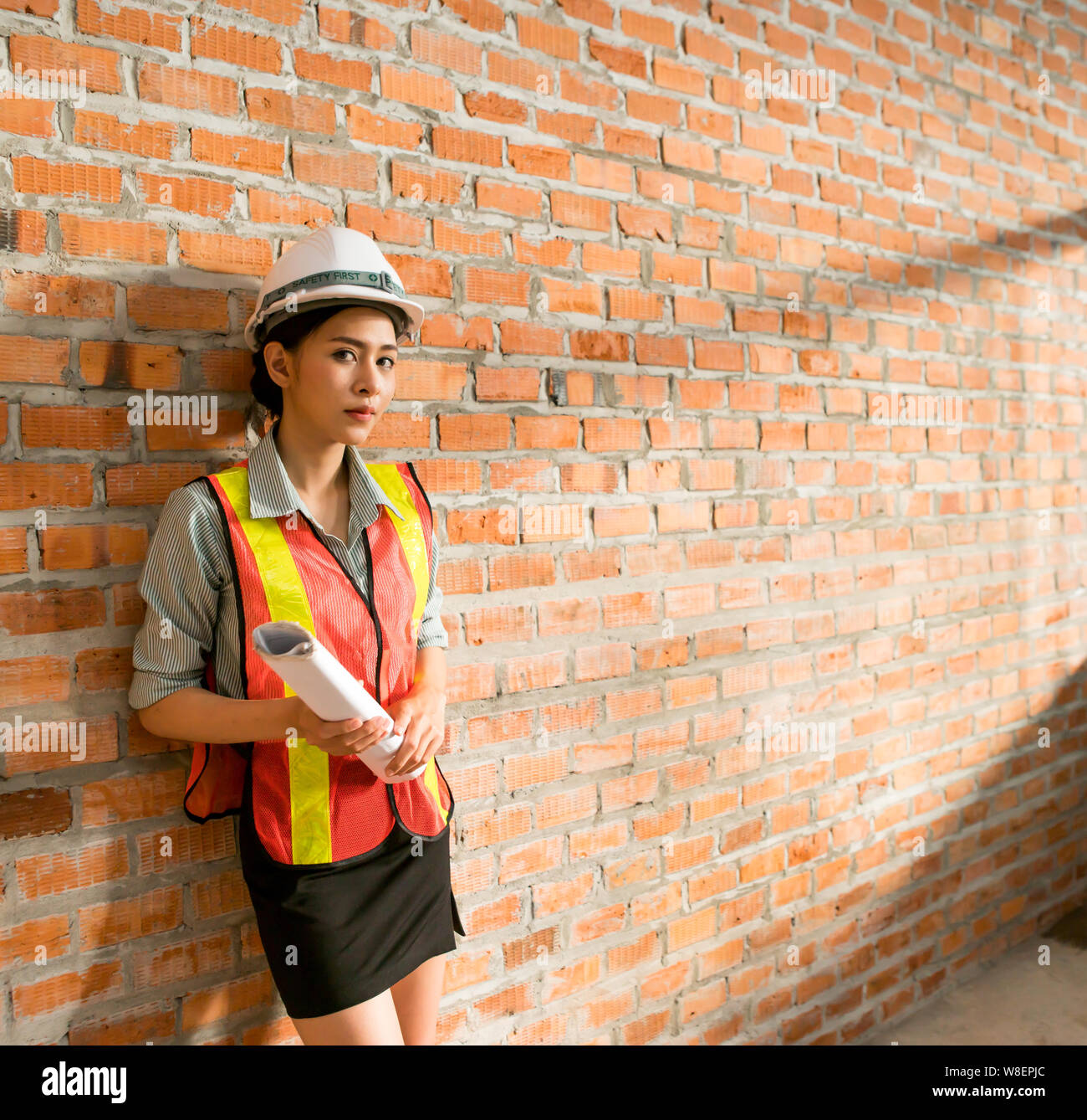 Ingegnere asiatica donna con blueprint con muro di mattoni in background Foto Stock