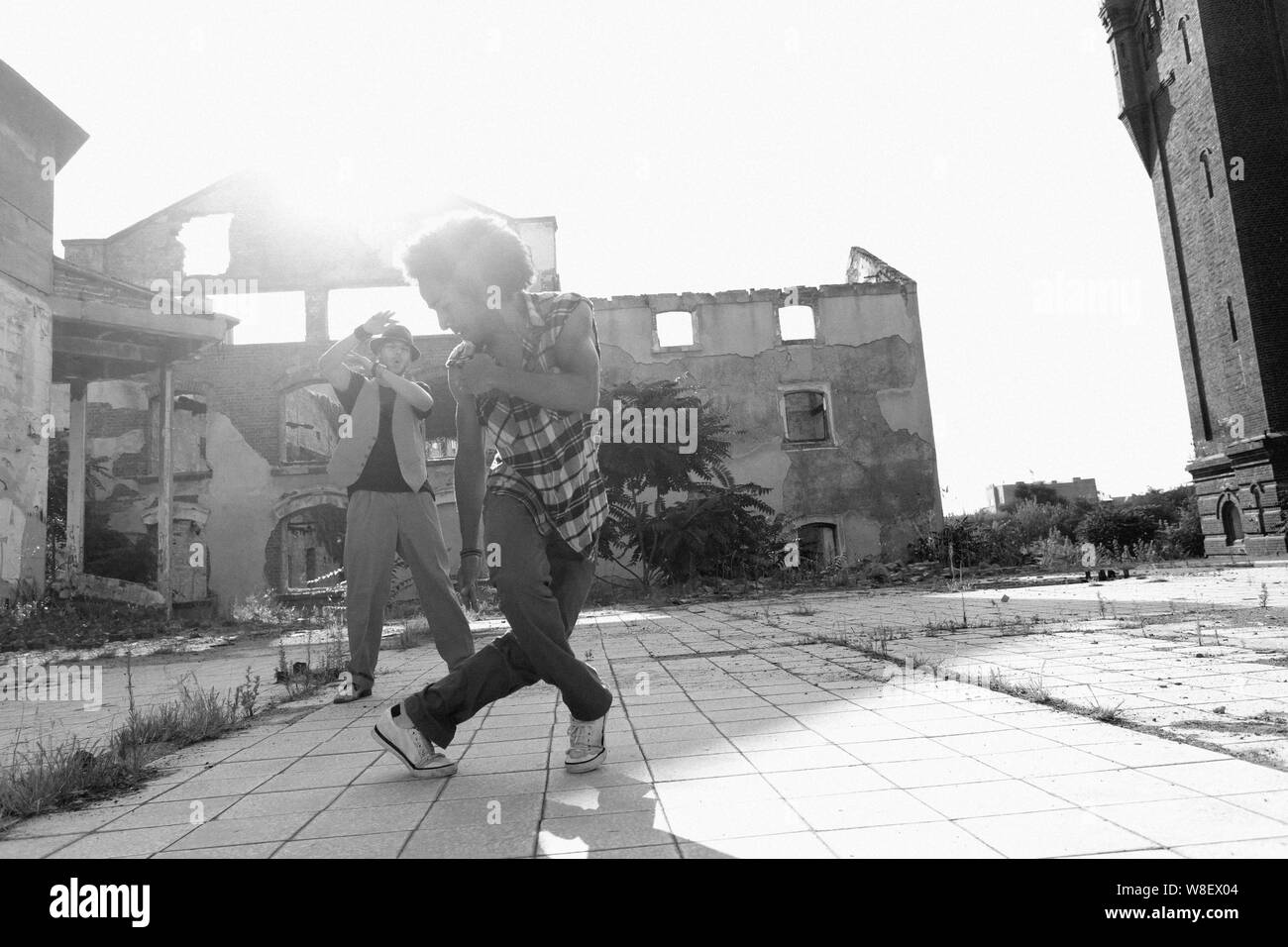 Giovane maschio americano africano hip hop o street dancer con ricci capelli afro eseguendo la sua energica dance routine in una piazza della città con il sole backlig Foto Stock