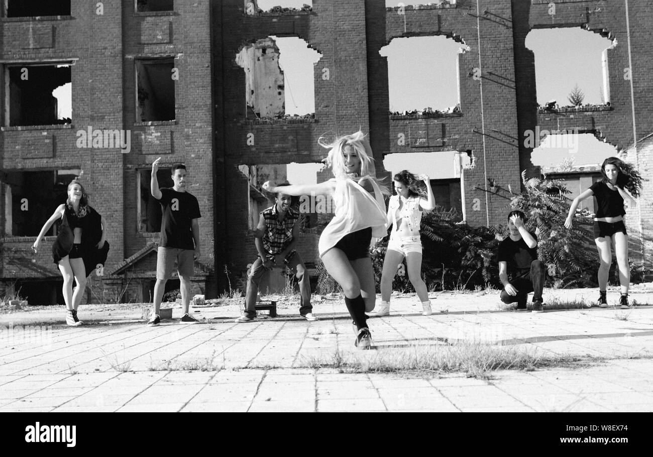 Ragazza giovane hip hop in una piazza con i suoi amici il suo supporto. La luce naturale del sole su edifici ad alta. Foto Stock