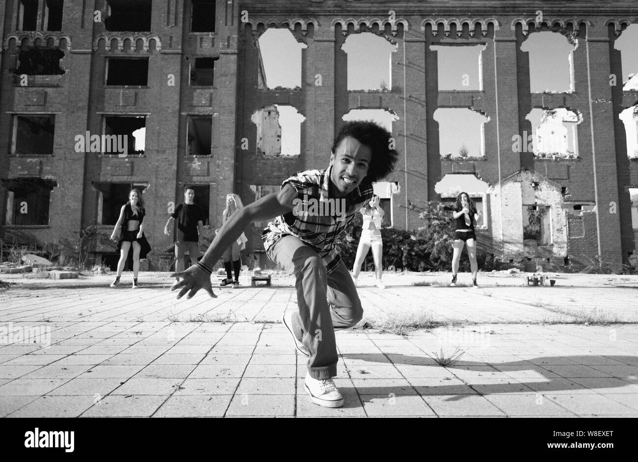 Felice energico African American street dancer allungandoti verso la telecamera con un sorriso impertinente come egli esegue la sua danza hip hop di routine in una piazza urbana. Foto Stock