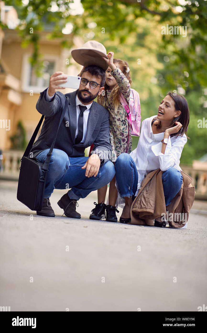 Primo giorno di scuola e genitori felici e ragazza facendo una foto di fronte a scuola Foto Stock