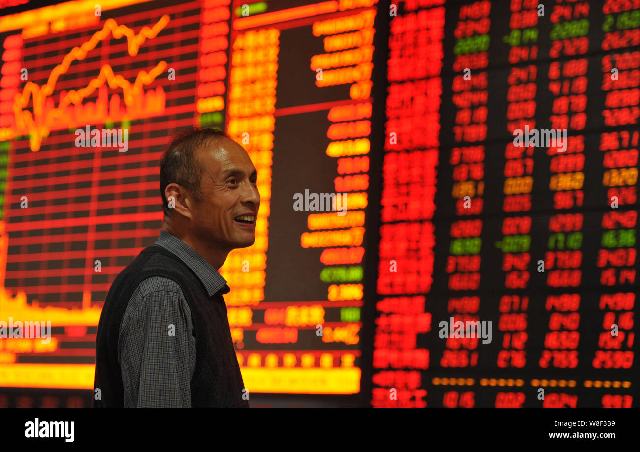 Un investitore cinese sorride come egli guarda gli indici azionari e i prezzi delle azioni (rosso per il prezzo in aumento e verde per la caduta dei prezzi) in corrispondenza di un magazzino di ho di brokeraggio Foto Stock