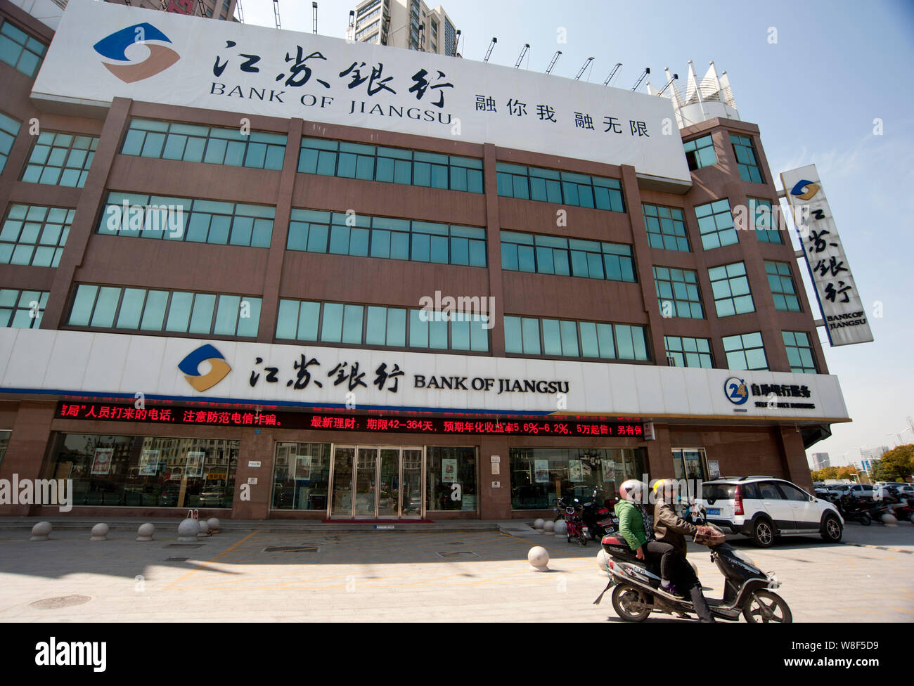 --FILE--ciclisti cinese di cavalcare una bicicletta elettrica passato una filiale della banca di Jiangsu nella città di Nantong, est cinese della provincia di Jiangsu, 6 aprile 2014. Banca o Foto Stock