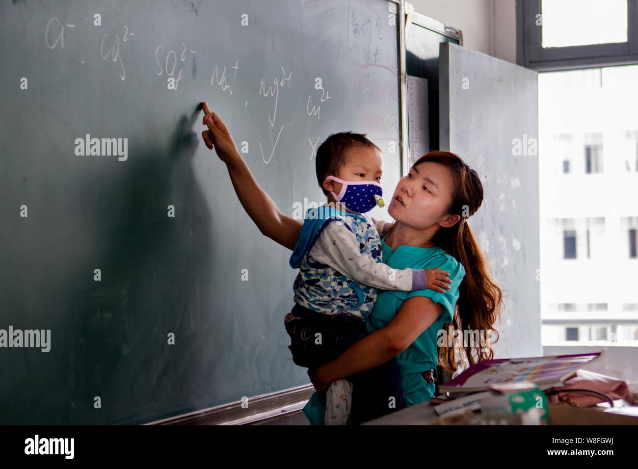 Zhang Wei porta il suo 3-anno-vecchio figlio Tutu, chi soffre di leucemia, mentre dà una lezione di chimica in un' aula a Hanshou n. 1 Alta scuola Foto Stock