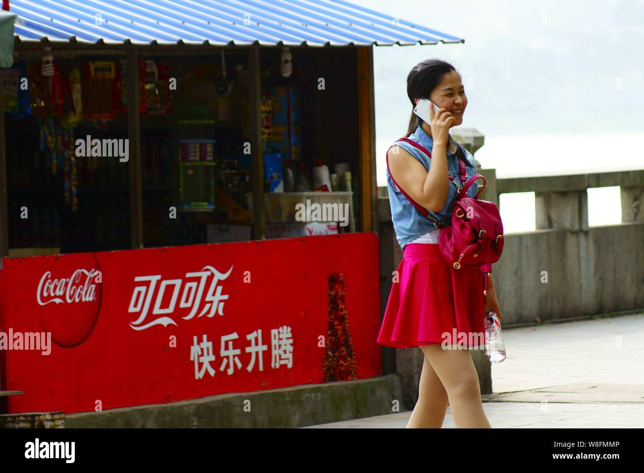 --FILE--un pedone usando il suo smartphone passeggiate passato un annuncio pubblicitario per la Coca Cola in Yichang city, centrale cinese della provincia di Hubei, 13 maggio 2015. Co Foto Stock