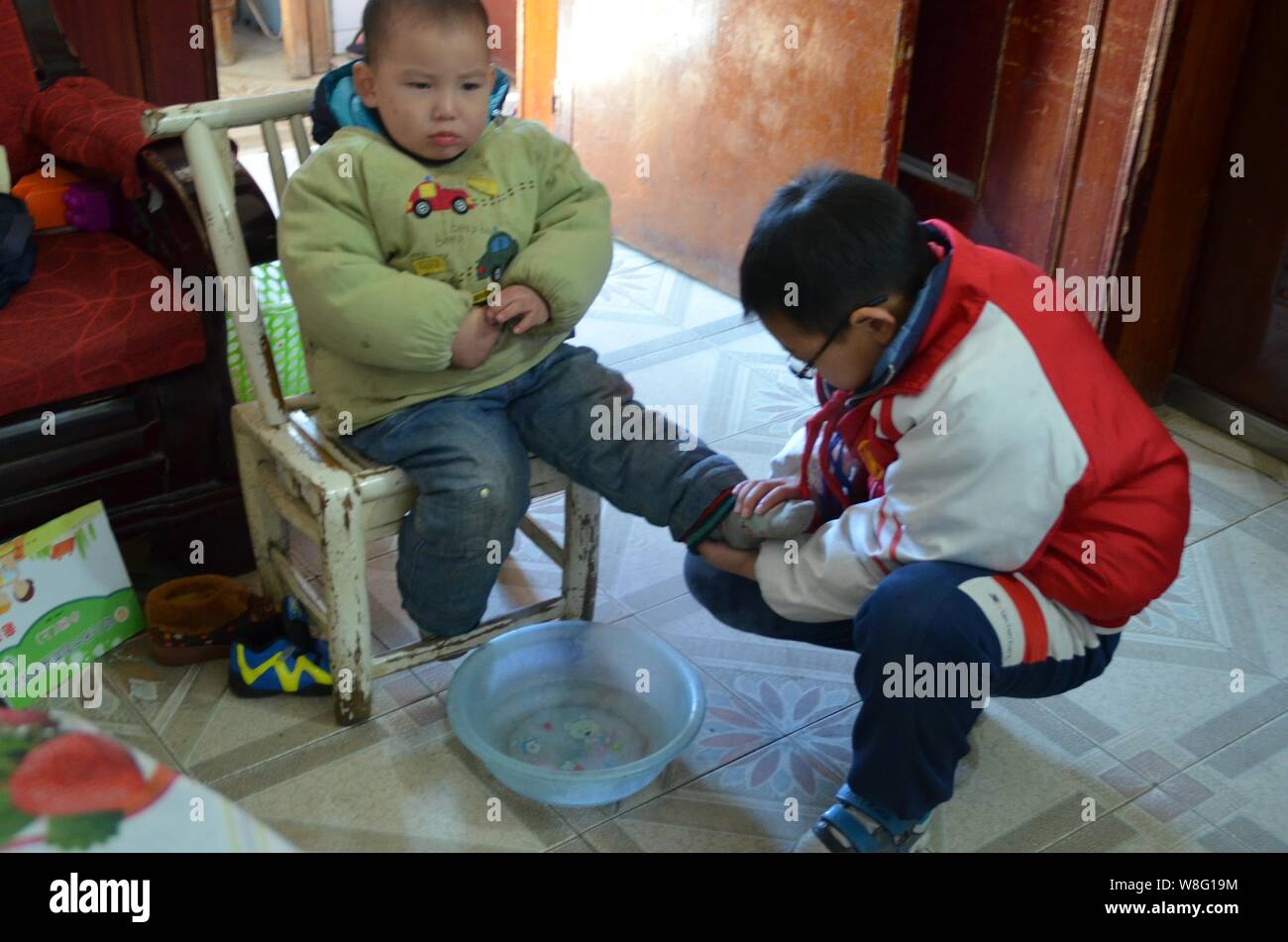 Il 10-anno-vecchio ragazzo Mo Shuangyi, destra lava il suo fratello più giovane i piedi a casa nella contea di Tonggu, Yichun city, Cina orientale della provincia di Jiangxi, 21 Dicembre Foto Stock