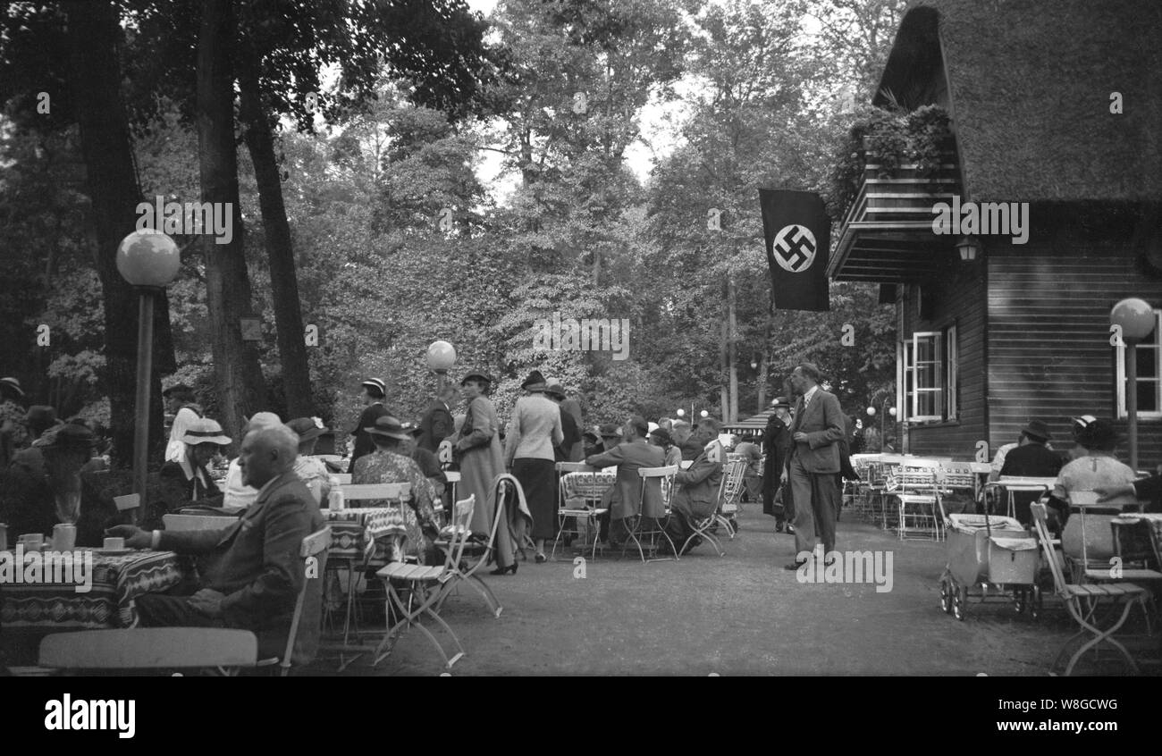 Le persone al di fuori-ristorante porta in Germania prima della outberak della II Guerra Mondiale, con bandiera nazista con la svastica emblema prominente sul display, 1930s Foto Stock