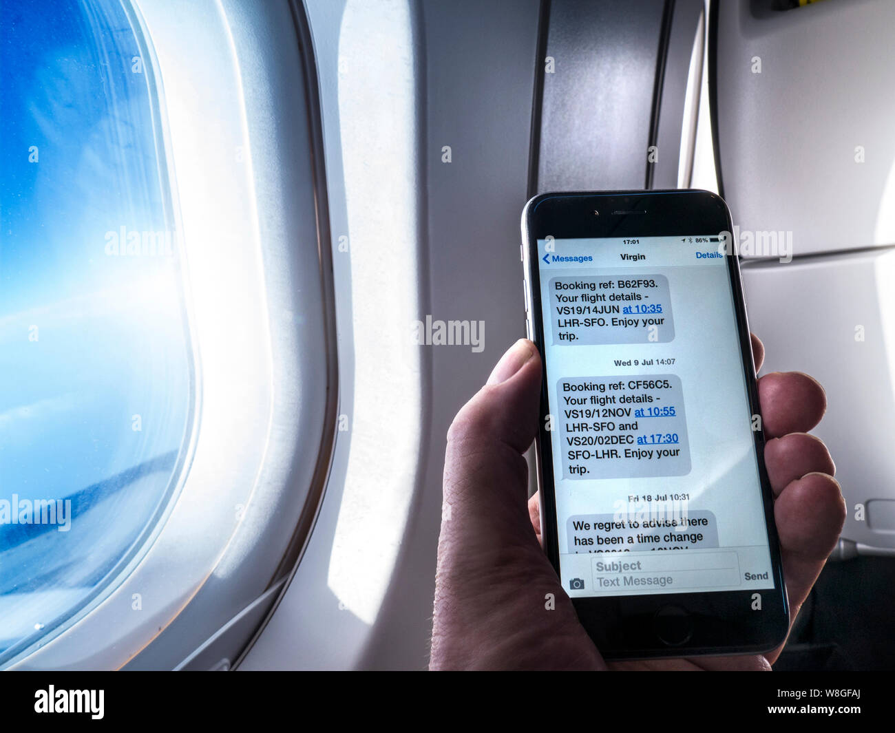 Smartphone Prenotazione volo Virgin Atlantic prenotazioni volo dettagli sullo schermo dello smartphone iPhone, mano e finestrino per aerei, app visualizzando un Virgin Atlantic prenotazione messaggio promemoria sullo schermo (dettagli alterato in modo sicuro) con cabina business class finestra a battente e cielo blu al di là Foto Stock