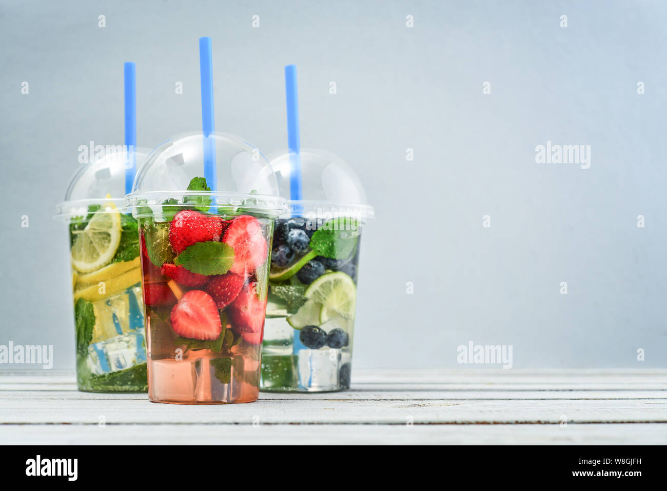 Varie La limonata con frutti e bacche in bicchieri di plastica con drink cannucce su sfondo blu. Tenere lontano il concetto di bevande. Foto Stock