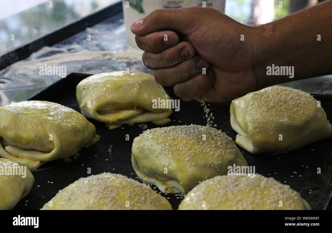 Una mano far cadere alcuni sesamo sulla parte superiore del pane pizza Foto Stock