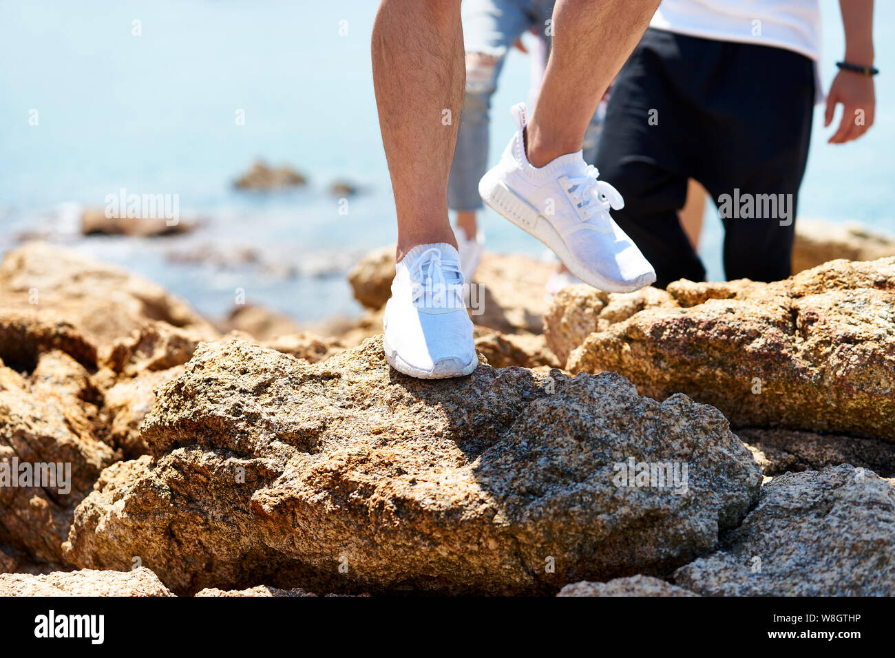 Close-up shot dei piedi del giovane uomo a camminare sulle rocce in riva al mare Foto Stock