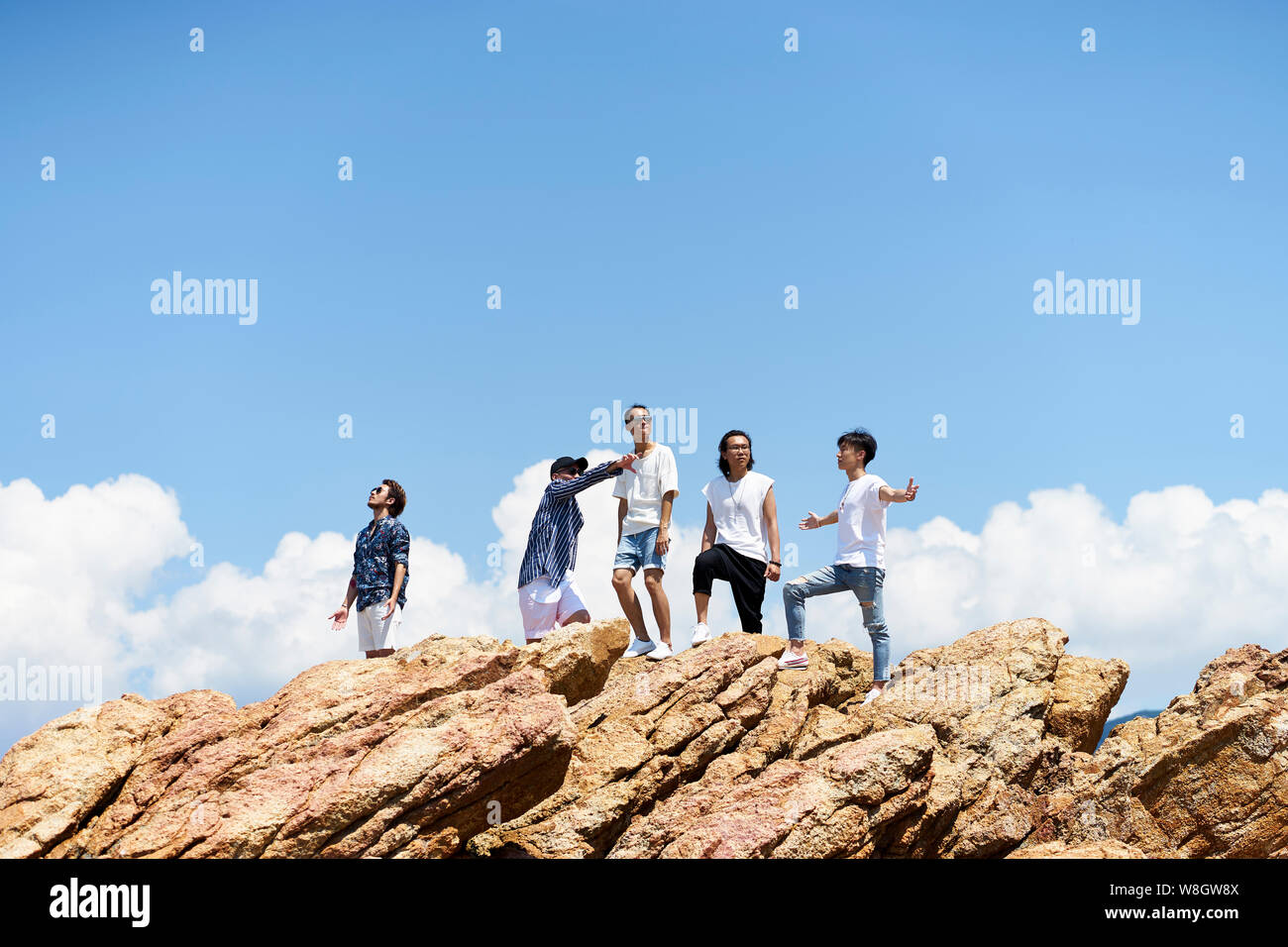 Un gruppo di giovani asiatici uomini adulti in piedi sulla parte superiore delle rocce contro il cielo blu godendo il sole e l'aria fresca Foto Stock