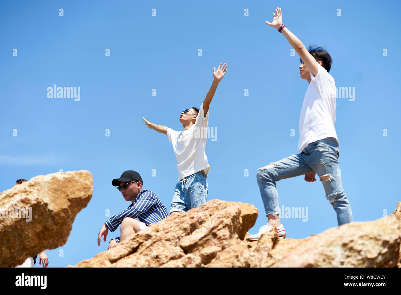 Un gruppo di giovani asiatici uomini adulti in piedi sulla parte superiore delle rocce contro il cielo blu godendo il sole e l'aria fresca Foto Stock