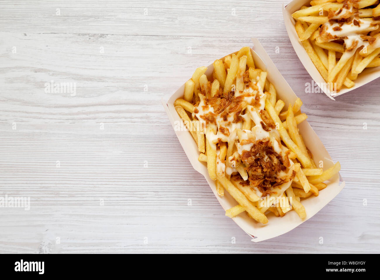 Un fast food: patatine fritte con salsa al formaggio e cipolle fritte in scatole di carta su un bianco sullo sfondo di legno, vista dall'alto. Spazio per il testo. Foto Stock