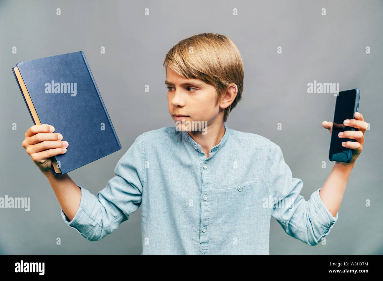 Kid facendo una dura scelta tra il libro e lo smartphone Foto Stock