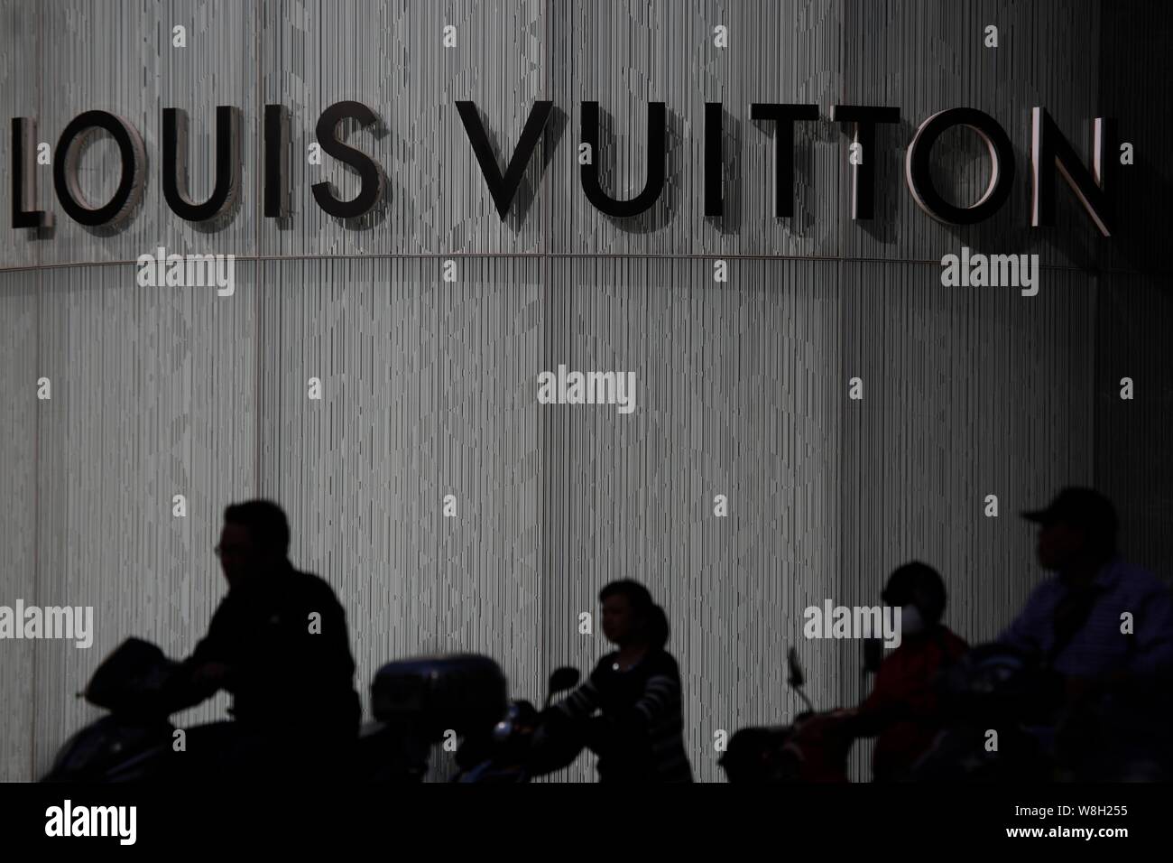 --FILE--ciclisti corsa biciclette elettriche passato una boutique alla moda di Louis Vuitton (LV) in Cina a Shanghai, 12 maggio 2015. Per contrastare il calo delle vendite in th Foto Stock