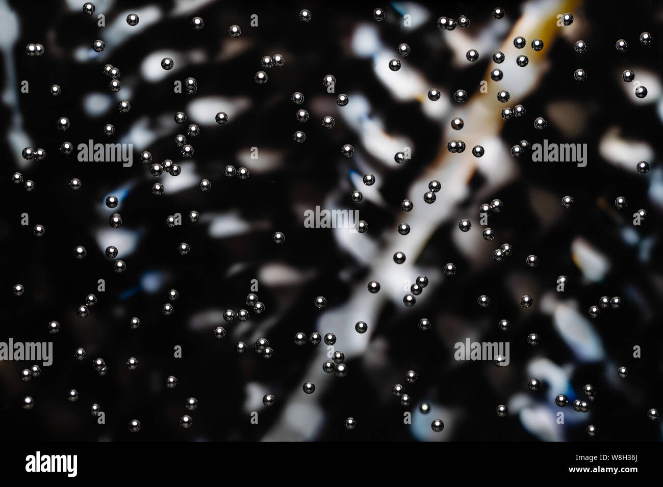 Centinaia di minuscoli cromato lucidato i cuscinetti a sfera a cascata verso il basso nella parte anteriore di un dolcemente focalizzata background industriale. I cuscinetti sono in calo in tutto il Foto Stock