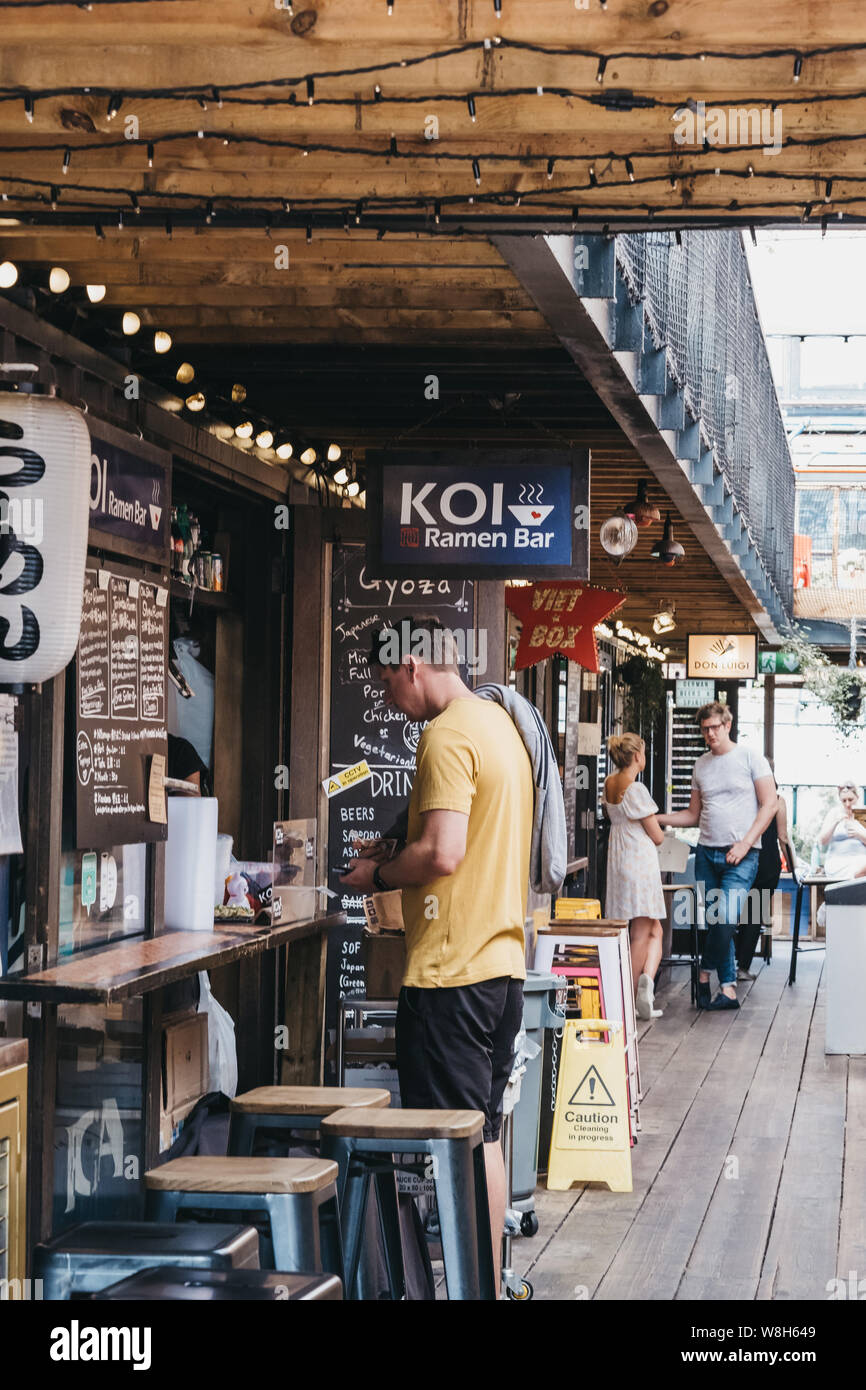 London, Regno Unito - 16 Luglio 2019:l'uomo ordinare del cibo da KOI Ramen in Pop Brixton, luogo dell'evento e la casa di una comunità di rivenditori indipendenti, restaura Foto Stock
