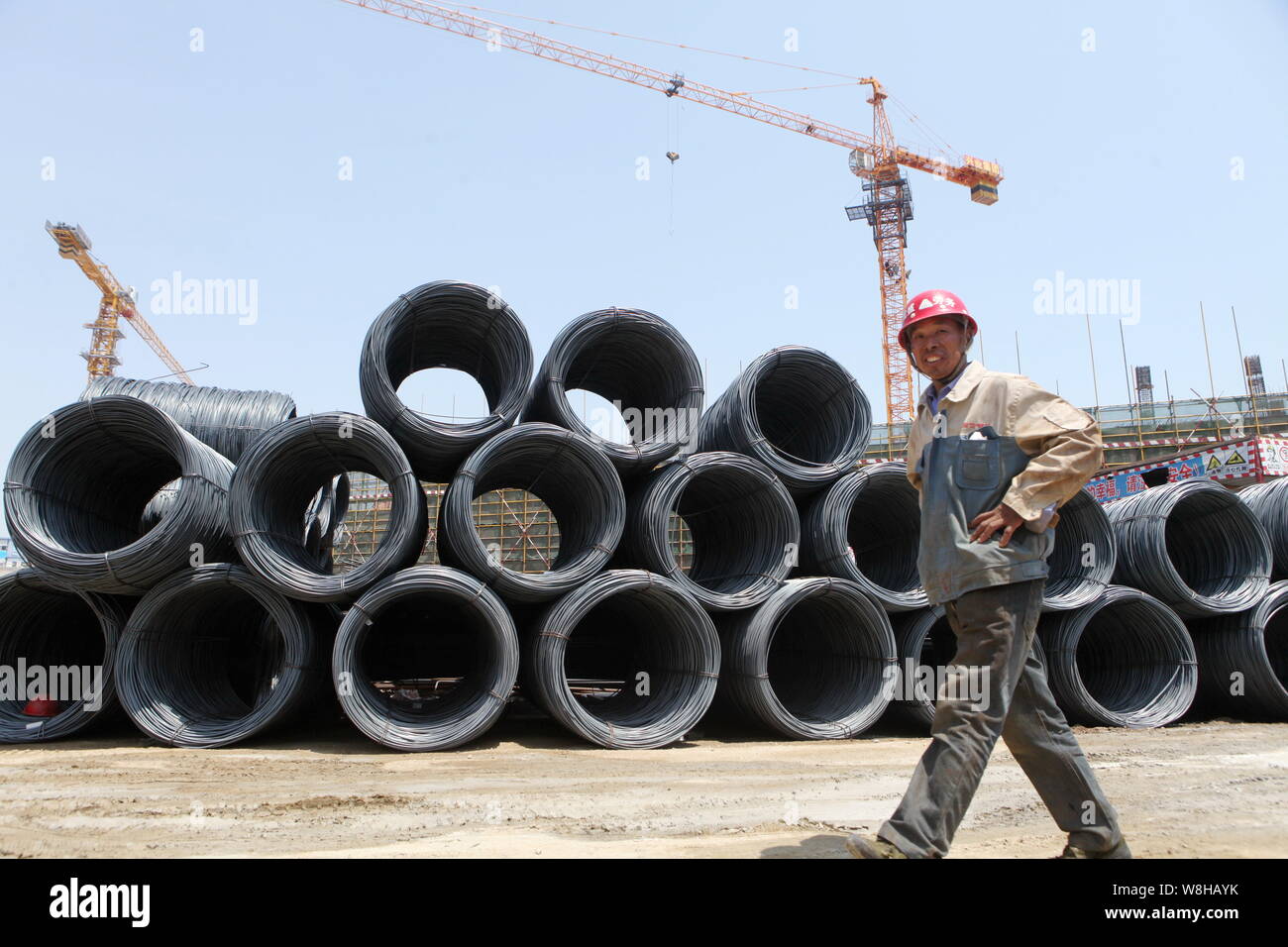 --FILE--un lavoratore cinese cammina davanti a un mucchio di spirale aste in acciaio in corrispondenza di un sito in costruzione nella città di Rizhao, est della Cina di provincia di Shandong, 9 maggio 2014. C Foto Stock