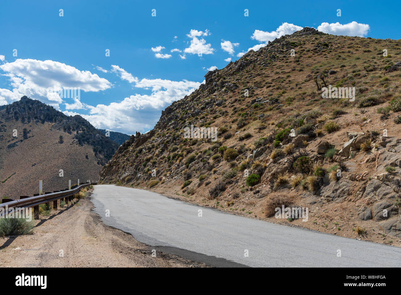 Deserto montagna in salita su strada asfaltata con guard rail sotto il cielo blu con nuvole bianche. Foto Stock