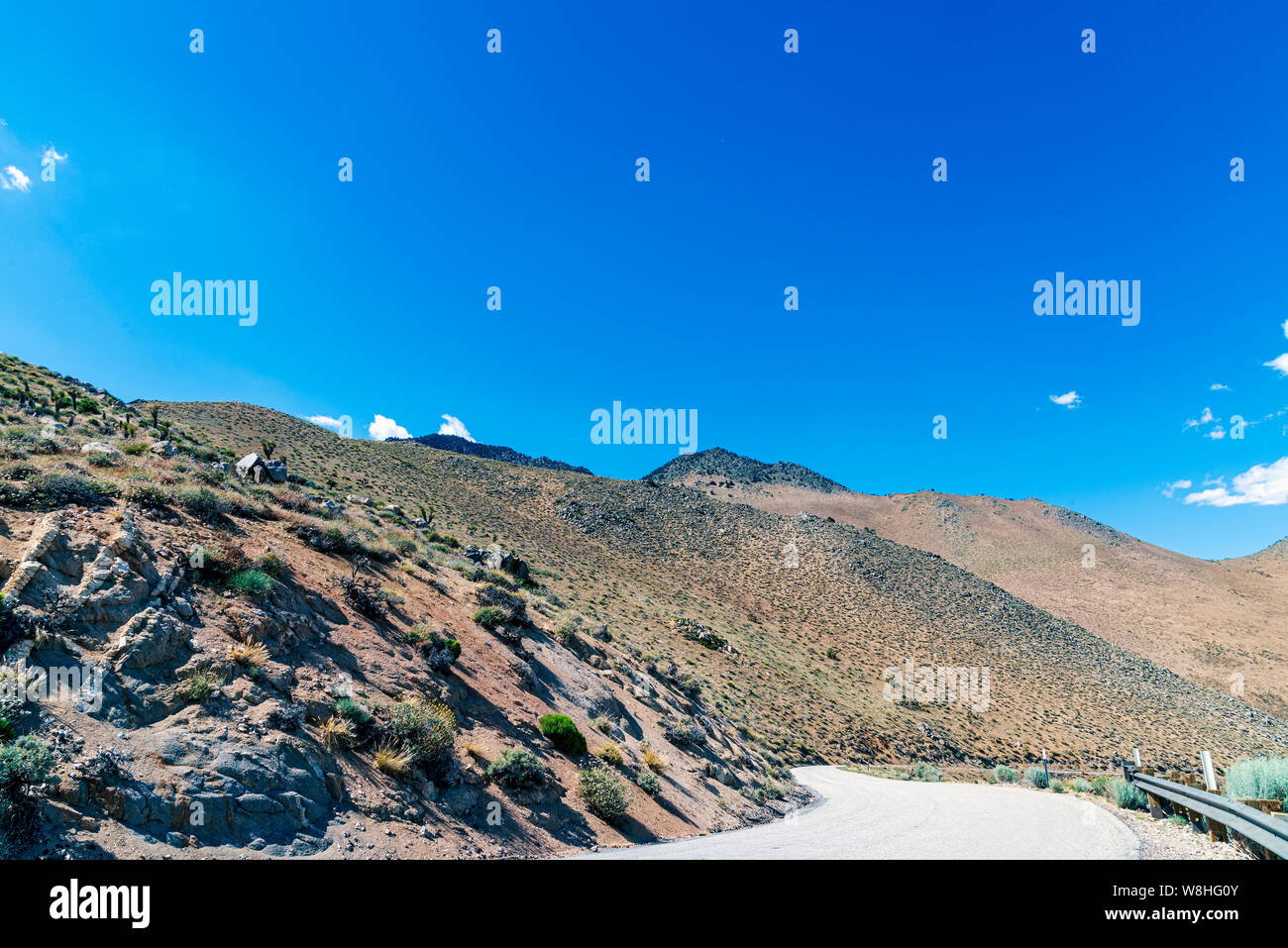 Pavimentato stretta strada di montagna che conduce giù la montagna con ringhiera. Deserto montagna rocciosa sotto il luminoso cielo blu. Foto Stock Pavimentato stretta strada di montagna che conduce giù la montagna con ringhiera. Deserto montagna rocciosa sotto il luminoso cielo blu. Foto Stock